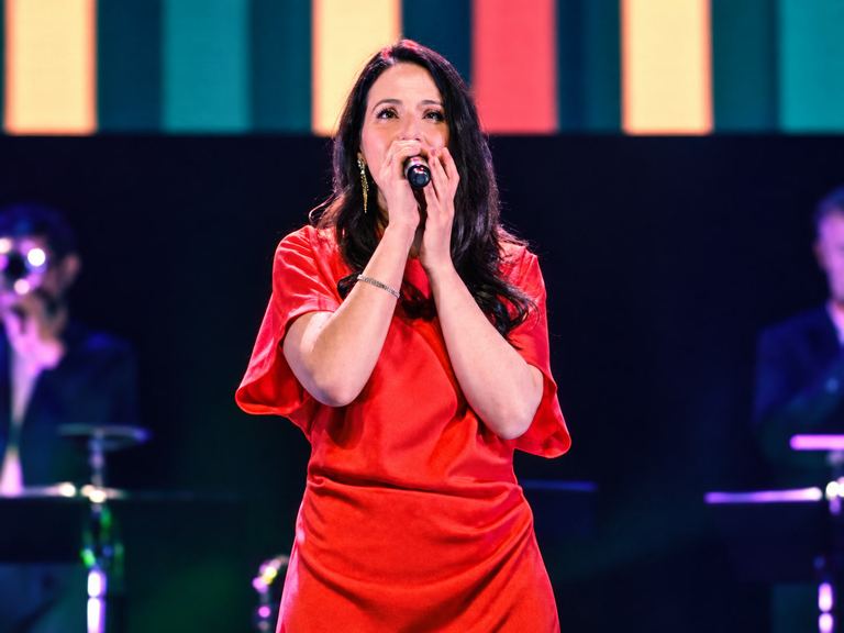 Isalia sur scène, micro à la main, en robe rouge